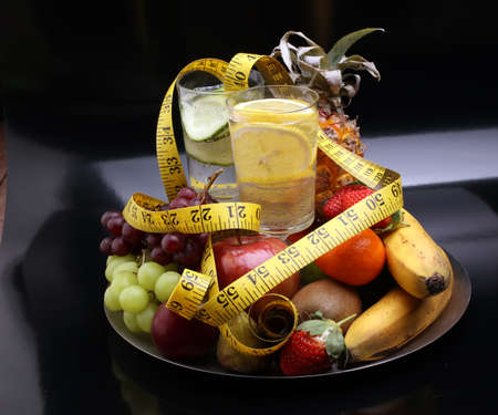 fitness equipment and healthy food and detox water (green apple, pepper, grapes, nectarines, kiwi, orange, dumbbells and measuring tape)の写真素材