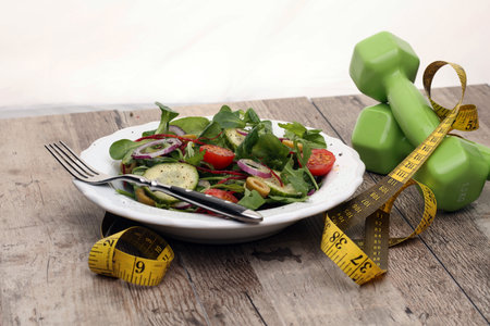 Fitness salad and measuring tape on rustic wooden table. Mixed greens, tomatos, diet cheese, olive...