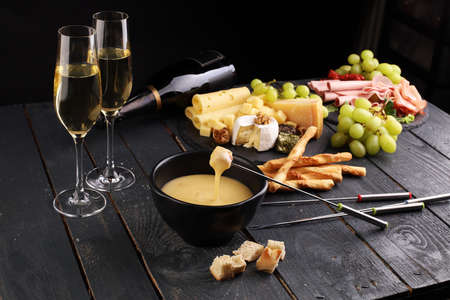 Gourmet Swiss fondue dinner on a winter evening with assorted cheeses on a board alongside a heated pot of cheese fondue with two forks dipping bread and white wine behind in a tavern or restaurantの写真素材