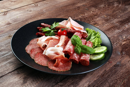 Food tray with delicious salami, pieces of sliced ham, sausage, tomatoes, salad and vegetable - Meat...