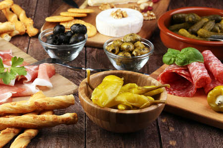 Italian antipasti wine snacks set. Cheese variety, Mediterranean olives, pickles, Prosciutto di Parma with melon, salami and wine in glasses over black grunge backgroundの写真素材