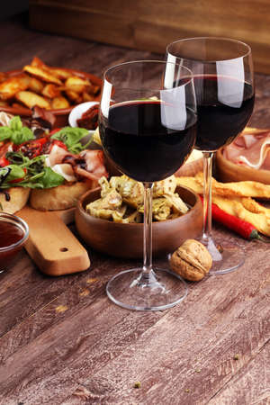Italian antipasti wine snacks set. Cheese variety, Mediterranean olives, pickles, Prosciutto di Parma, tomatoes, artichokes and wine in glasses over black grunge backgroundの写真素材