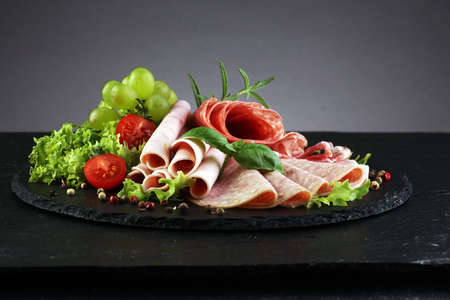 Food tray with delicious salami, pieces of sliced ham, sausage, tomatoes, salad and vegetable - Meat platter with selectionの写真素材