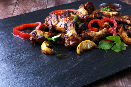 barbecue chicken wings close up on stone tray with pepper and limeの写真素材