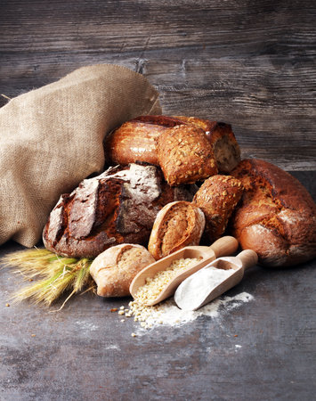 Different kinds of bread and bread rolls on board from above.