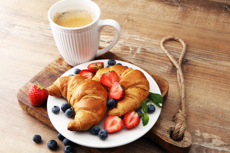 Delicious breakfast with fresh croissants and ripe berries on old wooden backgroundの写真素材
