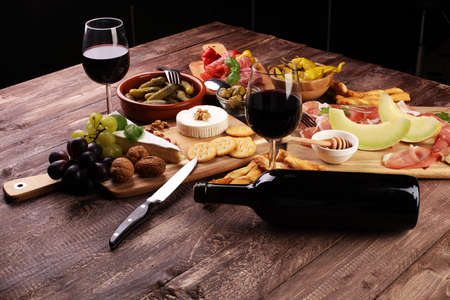 Italian antipasti wine snacks set. Cheese variety, Mediterranean olives, pickles, Prosciutto di Parma with melon, salami and wine in glasses over black grunge backgroundの写真素材