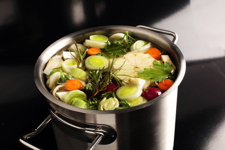 Broth with carrots, onions various fresh vegetables in a pot - colorful fresh clear spring soup....