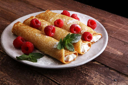 Homemade crepes served with fresh raspberrries and powdered sugar on rustic wooden tableの写真素材
