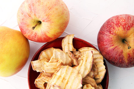 Dehydrated apples chips in bowl and apples on white background.の写真素材
