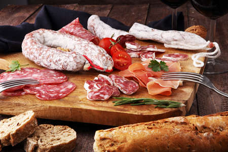Wooden cutting board with prosciutto, salami, sausages, wine, bread  and  rosemaryの写真素材