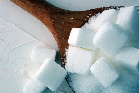 Cubes of sugar and granulated sugar with wooden spoon.