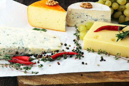 Different types of cheeses on board with walnut and grapes.