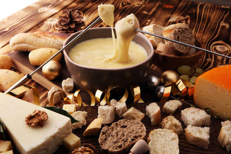 Gourmet Swiss fondue dinner on a winter evening with assorted cheeses on a board alongside a heated pot of cheese fondue with two forks dipping bread and white wine behind in a tavern or restaurant.の写真素材