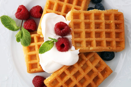 Plate of belgian waffles with whipped cream, mint and fresh berries