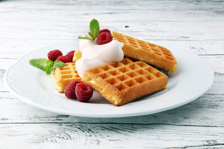 Plate of belgian waffles with whipped cream, mint and fresh berries