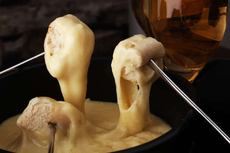 Gourmet Swiss fondue dinner on a winter evening with assorted cheeses on a board alongside a heated pot of cheese fondue with two forks dipping bread and white wine or champagneの写真素材