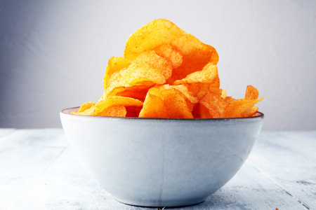 Crispy potato chips. Paprika chips on white wooden background