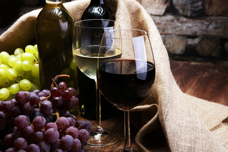 Red Wine bottle and white wine with grapes and glasses on wooden backgroundの写真素材