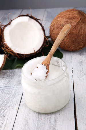 coconut and opened glass jar with fresh coconut oil on wooden background.