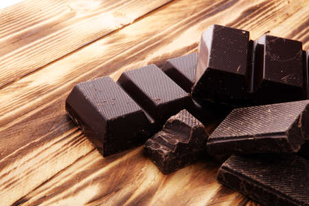 Dark brown chocolate pieces, stacks culinary wooden background.の写真素材