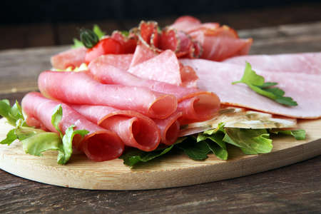 Food tray with delicious salami, pieces of sliced ham, sausage, tomatoes, salad and vegetable - Meat platter with selectionの写真素材