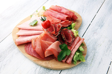 Food tray with delicious salami, pieces of sliced ham, sausage, tomatoes, salad and vegetable - Meat...