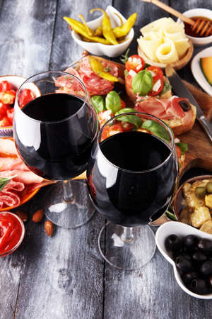 Italian antipasti wine snacks set. Cheese variety, Mediterranean olives, pickles, Prosciutto di Parma, tomatoes, artichokes and wine in glassesの写真素材