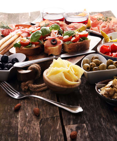 Italian antipasti wine snacks set. Cheese variety, Mediterranean olives, pickles, Prosciutto di Parma, tomatoes, artichokes and wine in glassesの写真素材