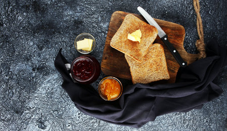 Toast bread with homemade strawberry jam and orange marmalade on rustic table served with butter for...