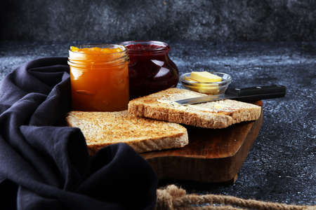 Toast bread with homemade strawberry jam and orange marmalade on rustic table served with butter for breakfast or brunch.の写真素材