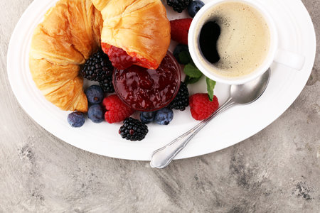 Delicious breakfast with fresh croissants, coffee and ripe berries on old marble backgroundの写真素材