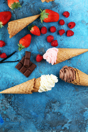 Vanilla frozen yogurt or soft ice cream in waffle cone and strawberry, raspberry and chocolate softice creamの写真素材