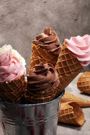 Vanilla frozen yogurt or soft ice cream in waffle cone and strawberry, raspberry and chocolate softice creamの写真素材