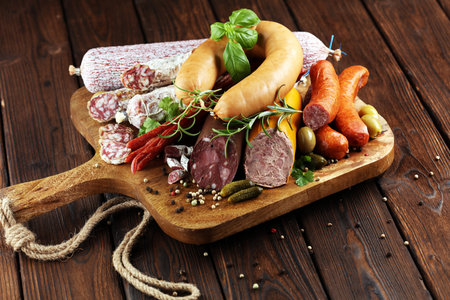 Food tray with delicious salami, ham,  fresh sausages, cucumber and herbs. Meat platter with...