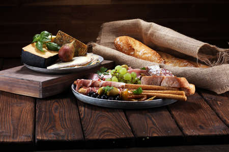 Italian antipasti wine snacks set. Cheese variety, Mediterranean olives, pickles, Prosciutto di Parma, salami and wine in glasses over black grunge backgroundの写真素材