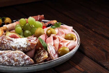 Italian antipasti wine snacks set. Cheese variety, Mediterranean olives, pickles, Prosciutto di Parma, salami and wine in glasses over black grunge backgroundの写真素材