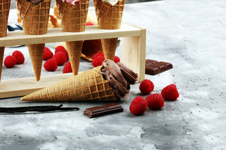 Vanilla frozen yogurt or soft ice cream in waffle cone and strawberry, raspberry and chocolate softice creamの写真素材