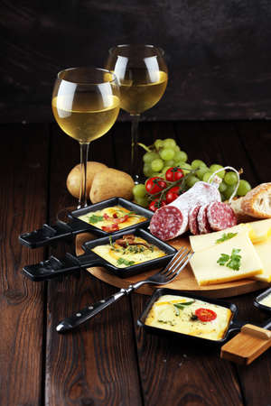 Delicious traditional Swiss melted raclette cheese on diced boiled or baked potato served in individual skillets with salami.の写真素材