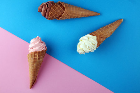 Vanilla frozen yogurt or soft ice cream in waffle cone flat lay on colored paper. 
