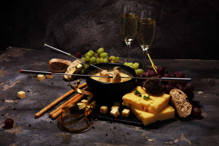 Gourmet Swiss fondue dinner on a winter evening with assorted cheeses on a board alongside a heated pot of cheese fondue with two forks dipping breadの写真素材