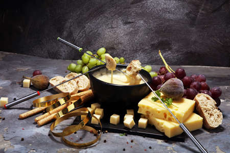 Gourmet Swiss fondue dinner on a winter evening with assorted cheeses on a board alongside a heated pot of cheese fondue with two forks dipping breadの写真素材