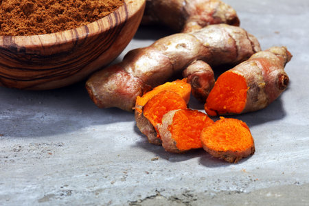 Turmeric powder and fresh turmeric on grey background.