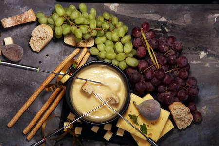 Gourmet Swiss fondue dinner on a winter evening with assorted cheeses on a board alongside a heated pot of cheese fondue with two forks dipping breadの写真素材