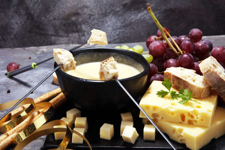 Gourmet Swiss fondue dinner on a winter evening with assorted cheeses on a board alongside a heated pot of cheese fondue with two forks dipping breadの写真素材