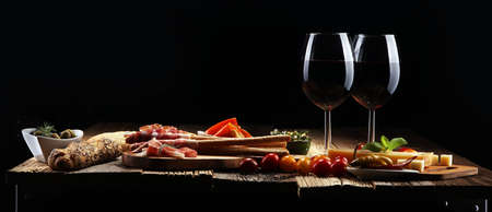 Italian antipasti wine snacks set. Cheese variety, Mediterranean olives, crudo, Prosciutto di Parma, salami and wine in glasses over wooden grunge backgroundの写真素材