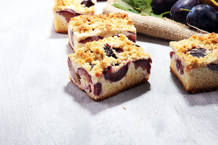Rustic plum cake on wooden background with plums around