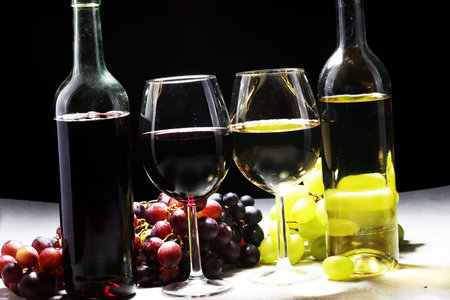 White wine and red wine in a glass with fall grapes, white stone background