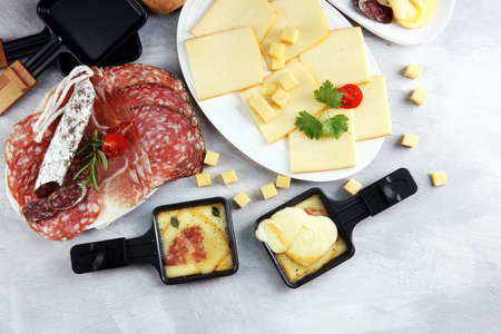 Delicious traditional Swiss melted raclette cheese on diced boiled or baked potato served in individual skillets with salami.の写真素材