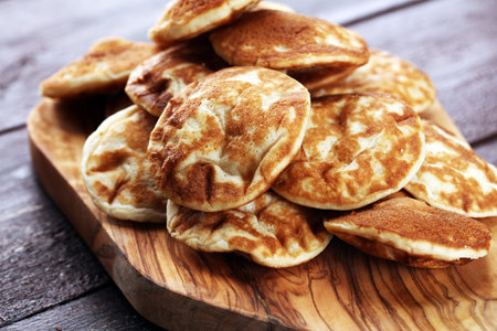 Pancakes or puffertjes with berries and maple syrup on rustic table.